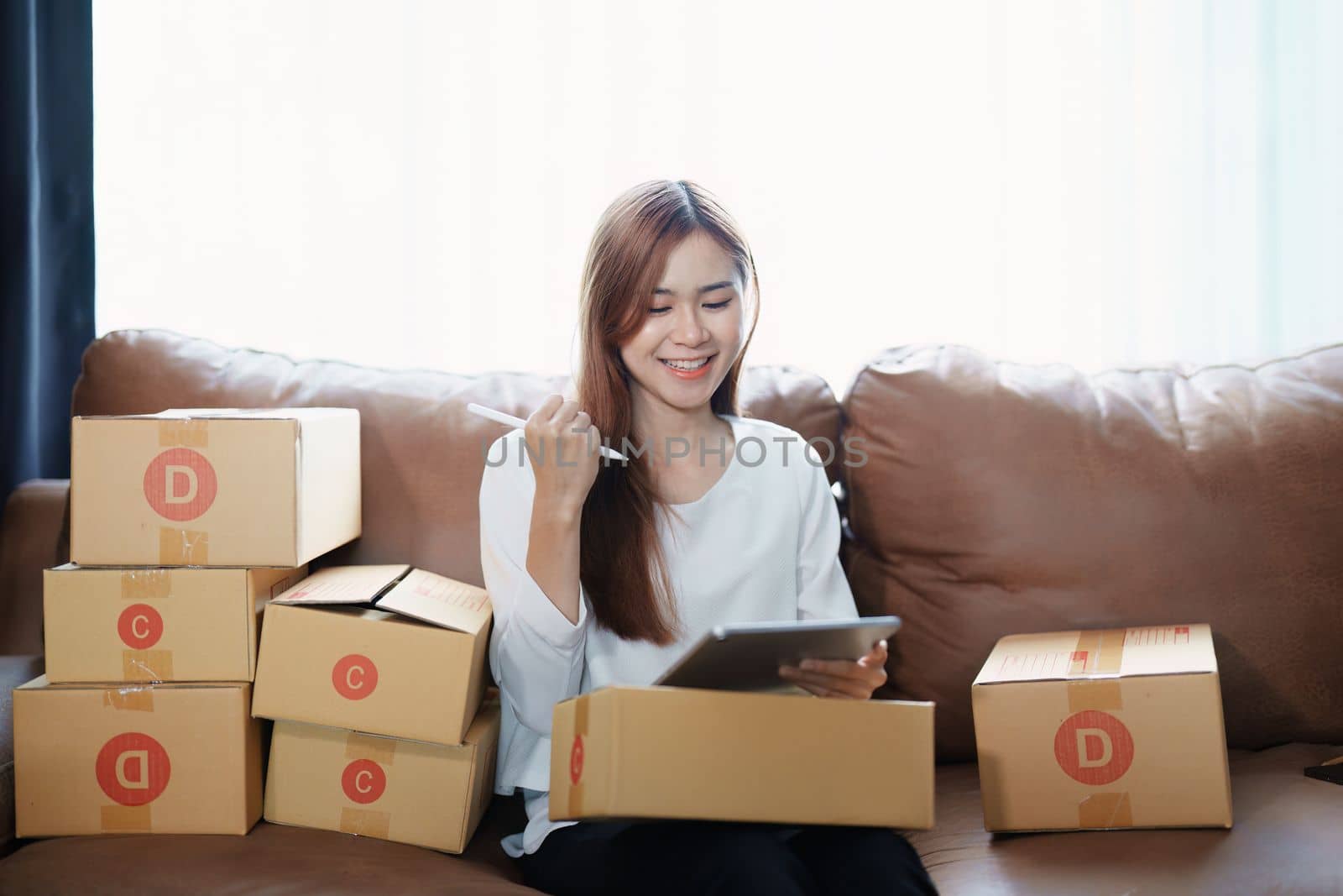 Starting small business entrepreneur of independent young Asian woman online seller is using tablet computer and taking orders to pack products for delivery to customers. SME delivery concept by Manastrong