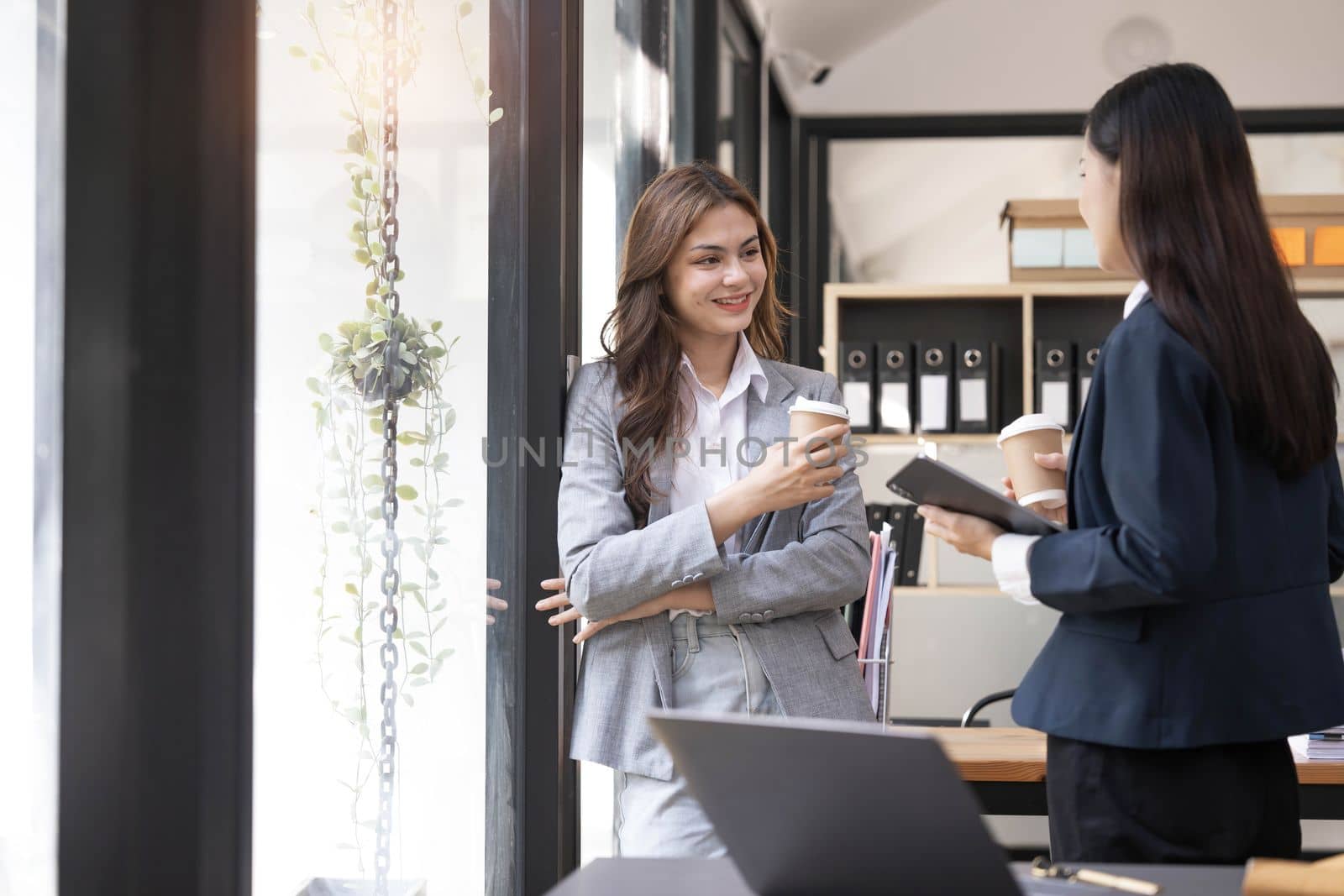 Happy two young Asian business woman holding coffee cup in coworking office by wichayada