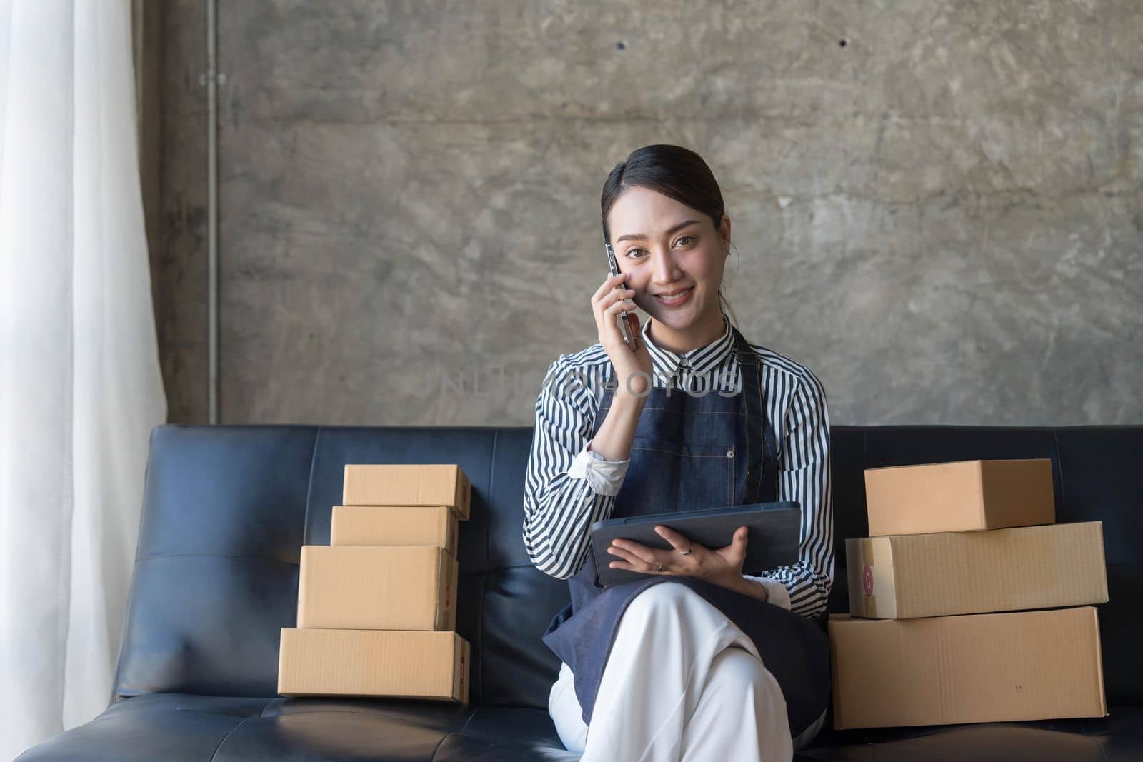 Startup small business entrepreneur SME freelance woman work with smart phone, Young Asian small business owner use computer, online market packing box delivery, SME e-commerce telemarketing concept..