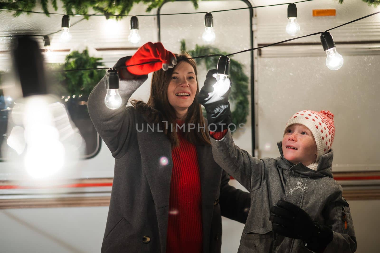 Caucasian woman and son decorate camper for christmas. Happy family travels in a mobile home