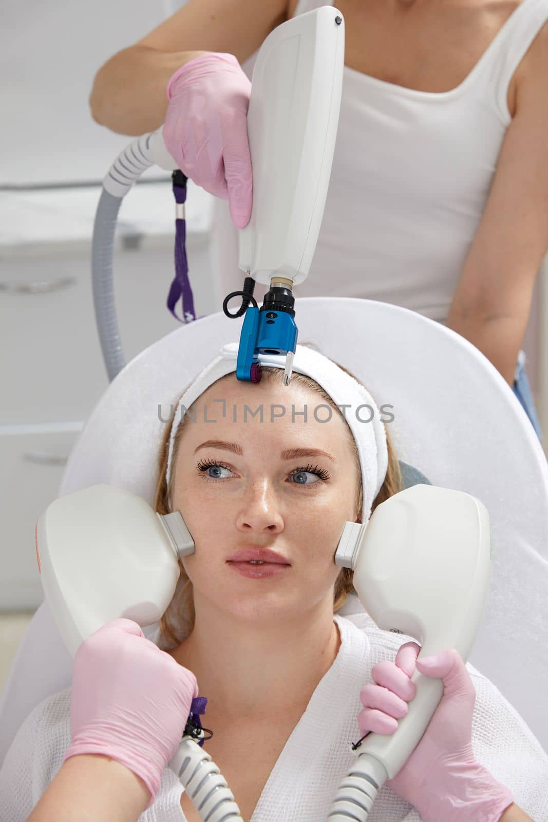 Conceptual beauty and cosmetology image of hands of several doctors holding laser equipment over female face. Cosmetology concept