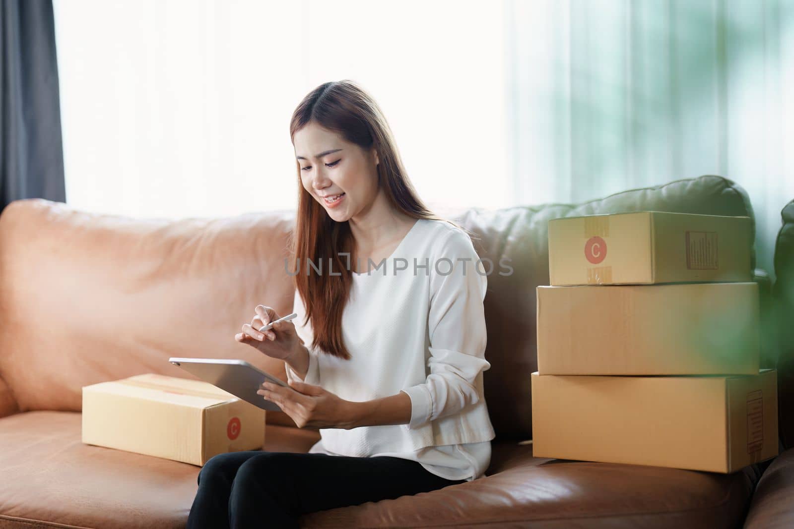 Starting small business entrepreneur of independent young Asian woman online seller is using tablet computer and taking orders to pack products for delivery to customers. SME delivery concept by Manastrong