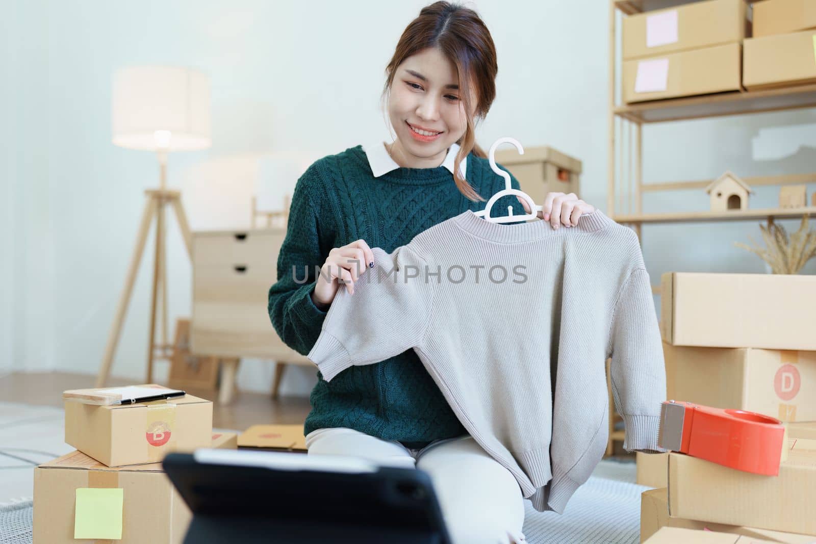 Starting small business entrepreneur of independent young Asian woman online seller using a tablet computer showing products to a customer before making a purchase decision. SME delivery concept.