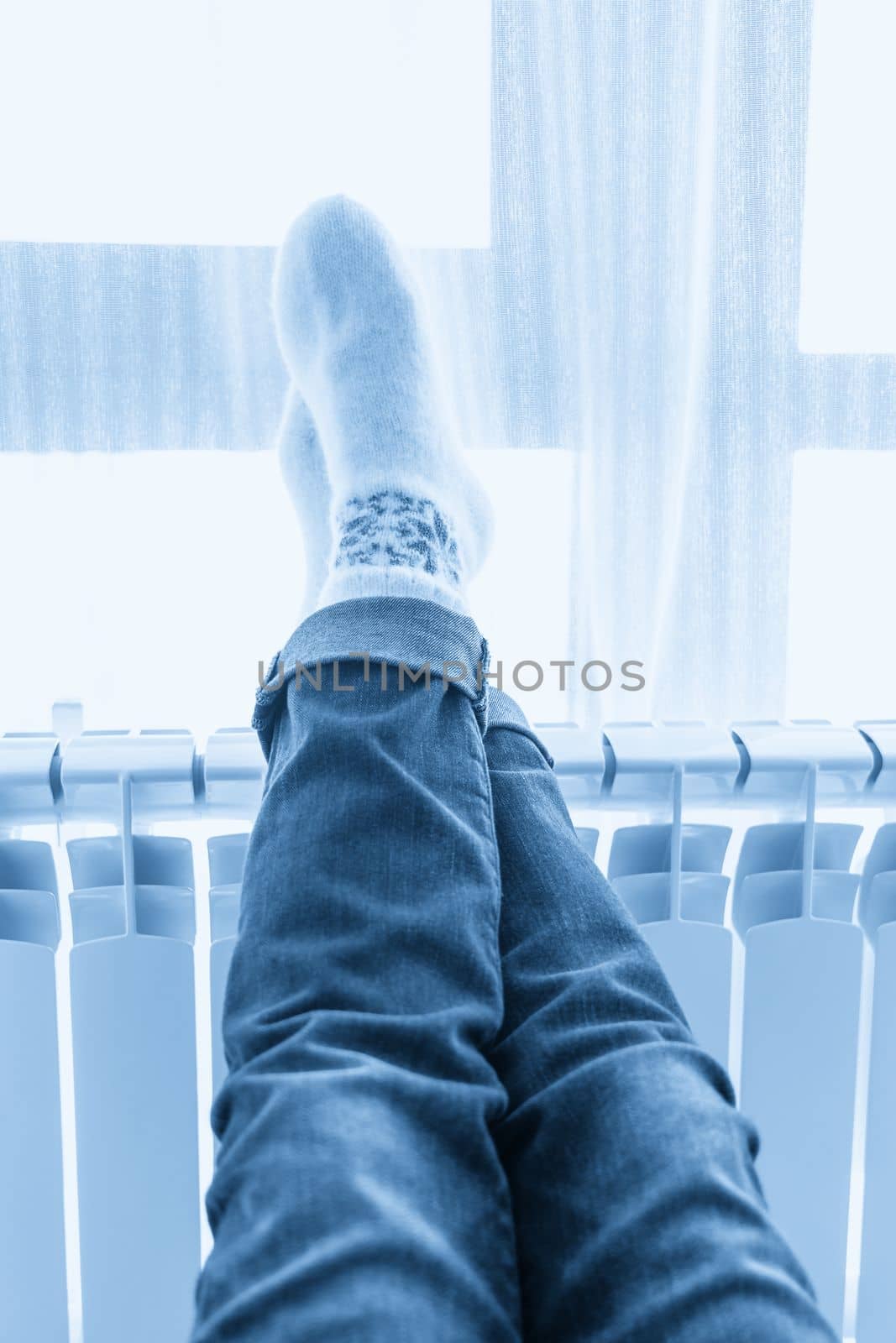 Woman warming up with feet on heater wearing woolen socks by Mariakray