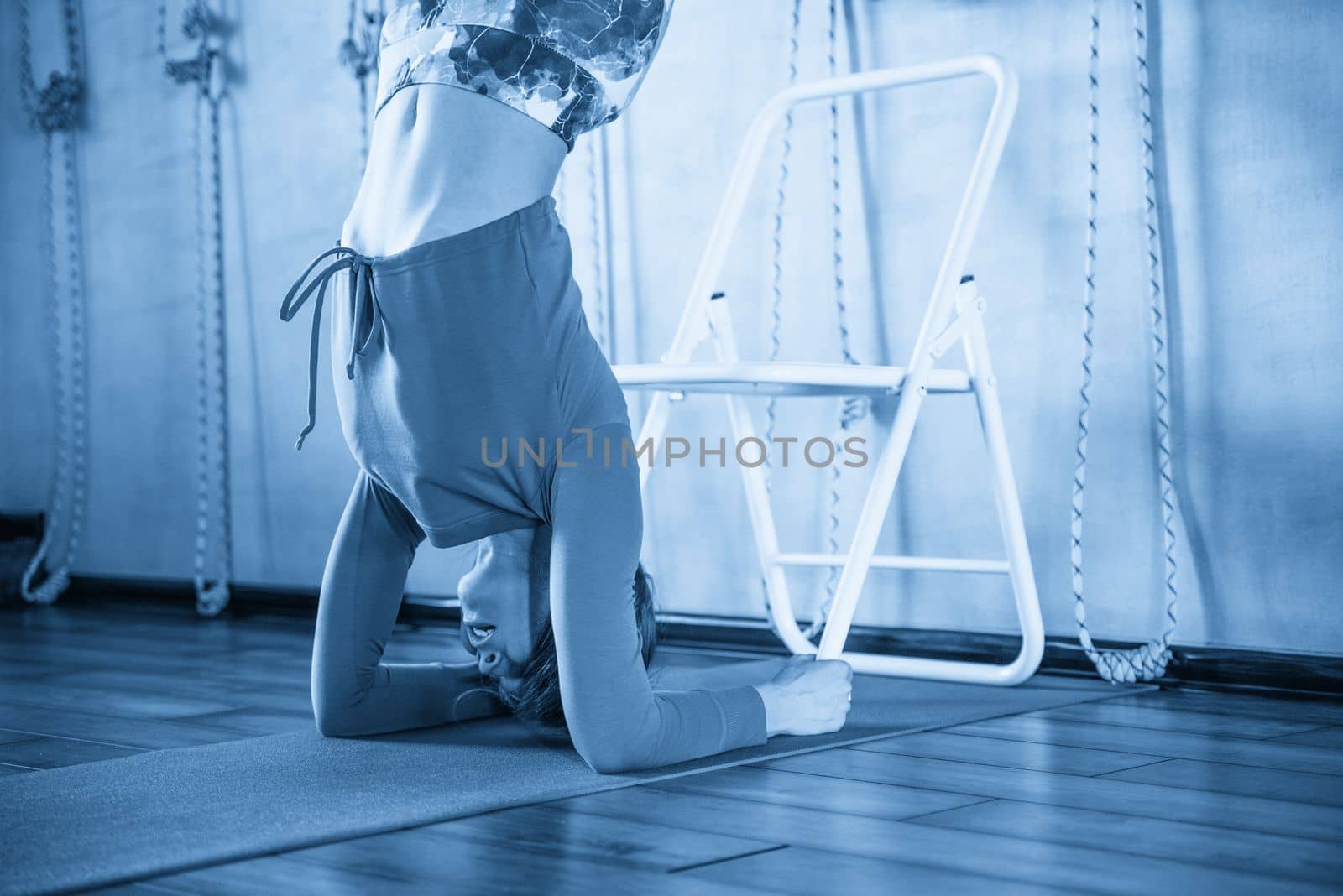 Sporty beautiful young woman practicing yoga, doing variation of Bridge Pose on elbows with chair