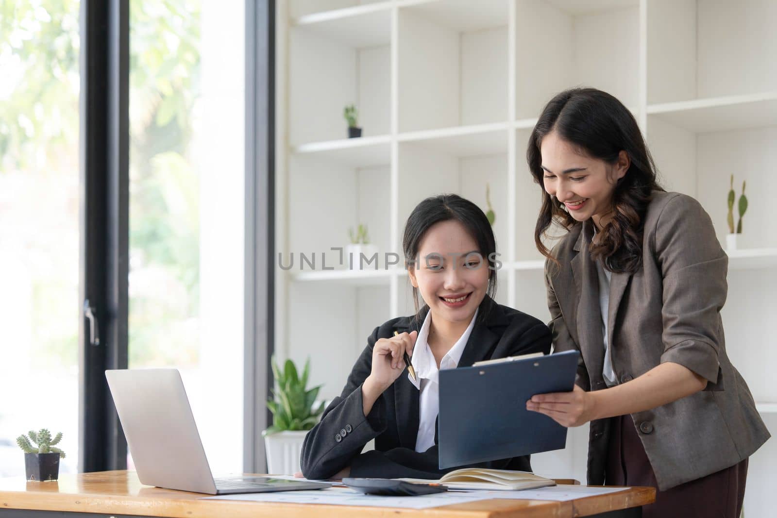 Two young Asian business woman talk, consult, discuss working with new startup project idea presentation analyze plan marketing and investment in the office. by wichayada