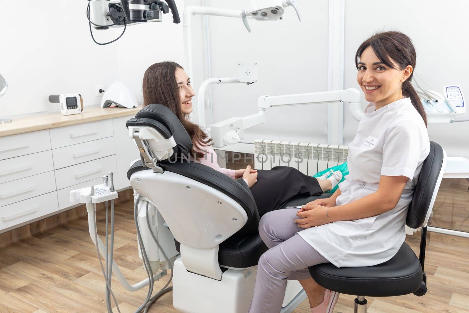 Female dentist talking to a young patient during appointment in modern dental clinic before teeth treatment by Mariakray