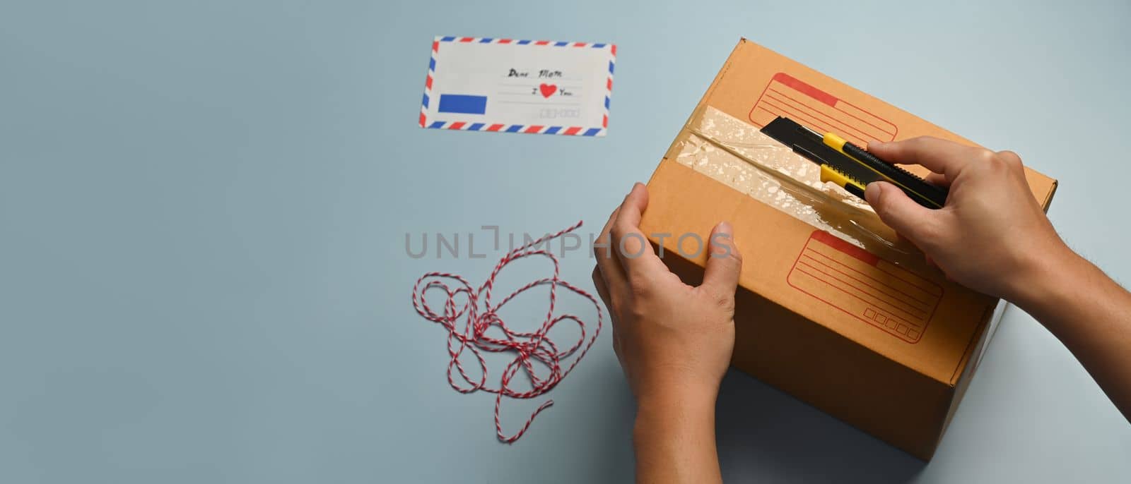 Overhead view of man cutting a cardboard box with sharp cutter knife. Delivery and online shopping concept.