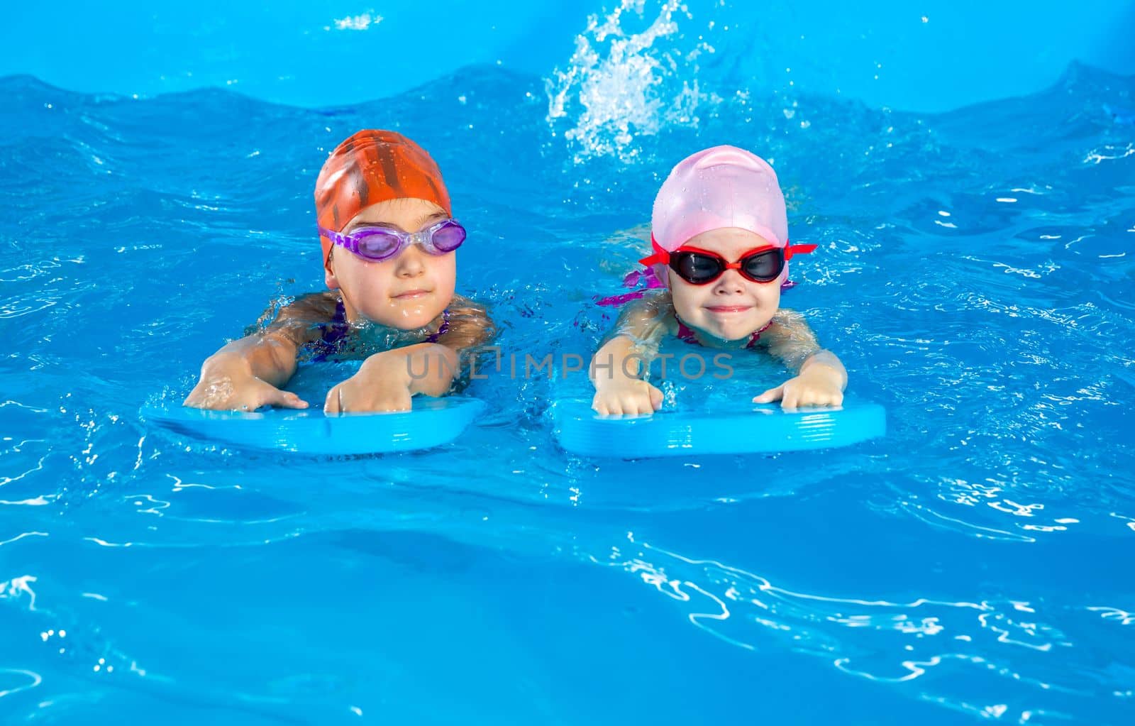 Two little girls having fun in pool learning how to swim using flutter boards by Mariakray