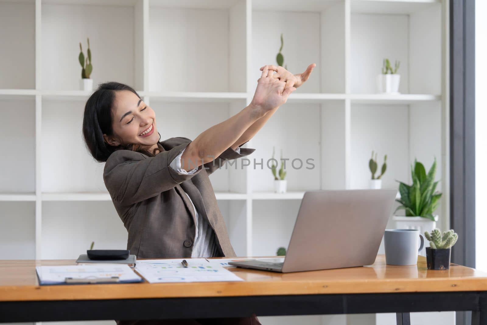 Asian businesswoman stretches her arms to relax her tired muscles from working at her desk all day at the office...