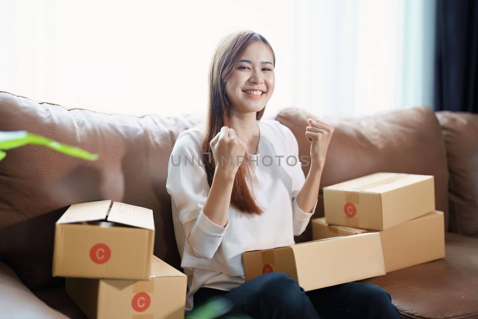 Starting small business entrepreneur of independent Asian woman smiling using computer laptop with cheerful success of online marketing package box items and SME delivery concept by Manastrong