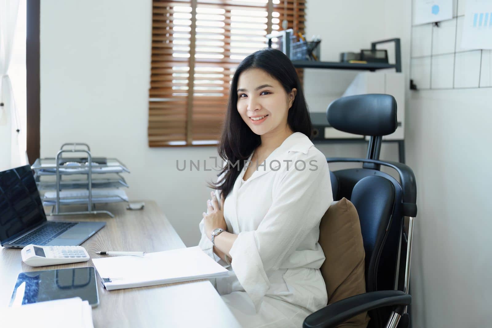 Portrait of a woman business owner showing a happy smiling face as he has successfully invested her business using computers and financial budget documents at work.