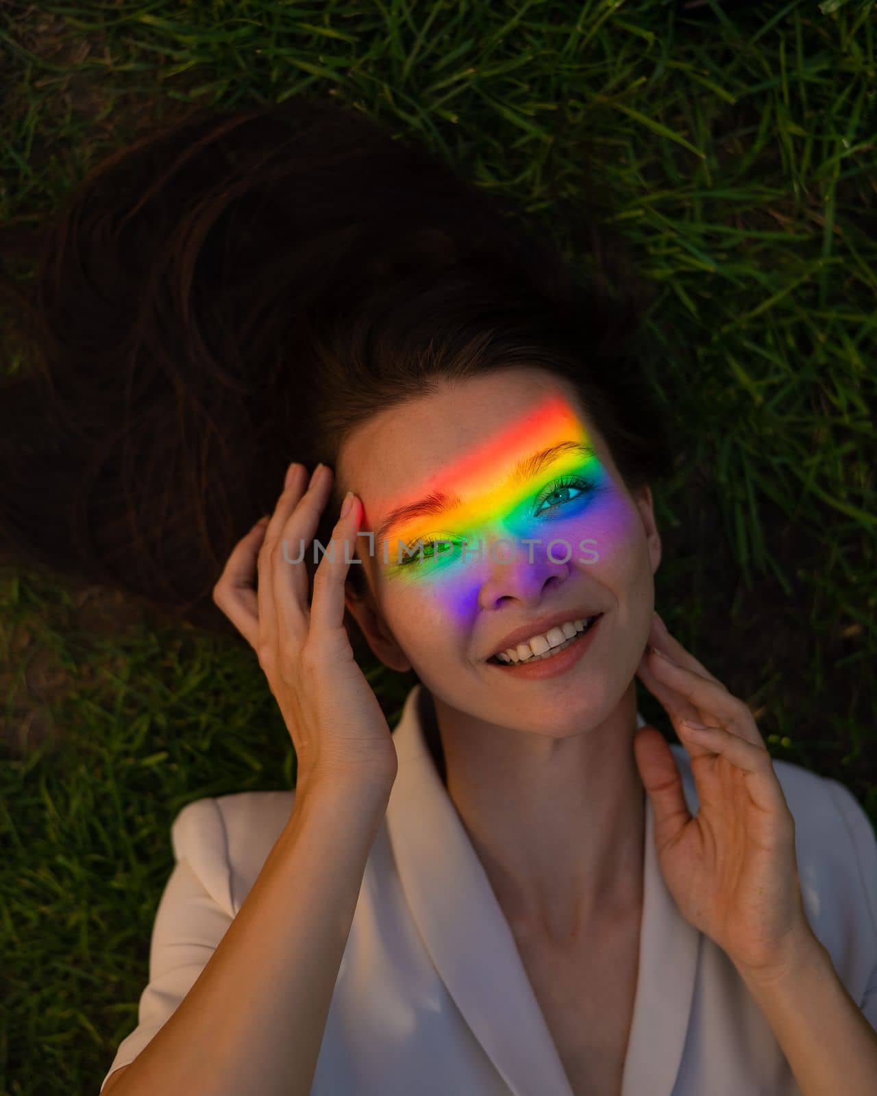 Top view of caucasian woman with rainbow ray on her face lies on green grass