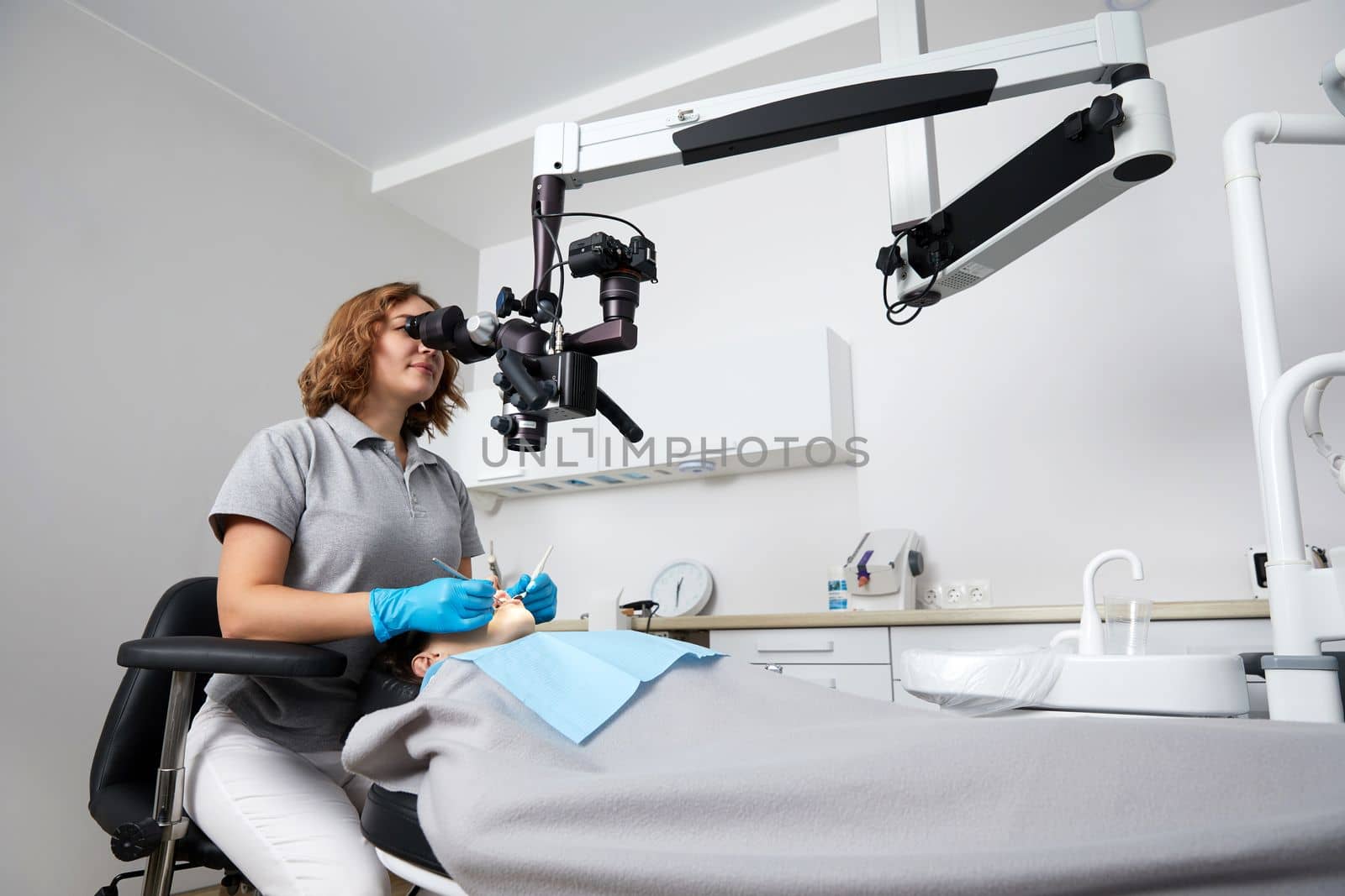 Female dentist with dental tools and microscope treating patient teeth at dental clinic office. Medicine, dentistry and health care concept. Dental equipment