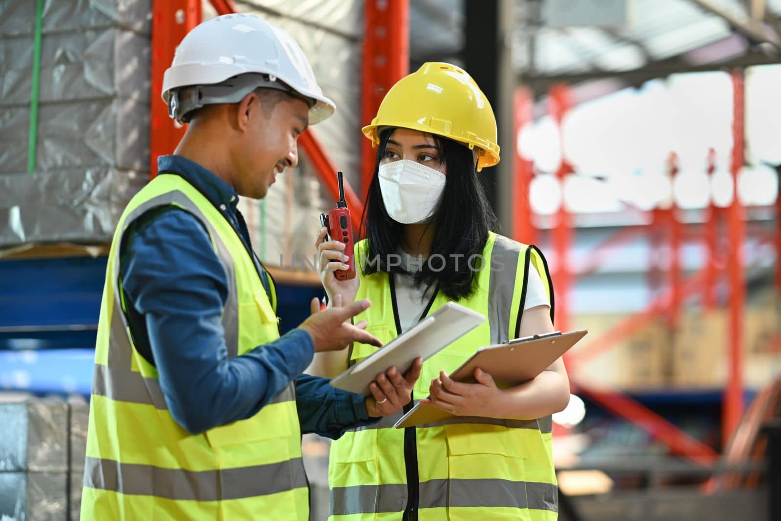 Female manager and male workers are checking order details on a tablet while standing between retail warehouse full of shelves by prathanchorruangsak