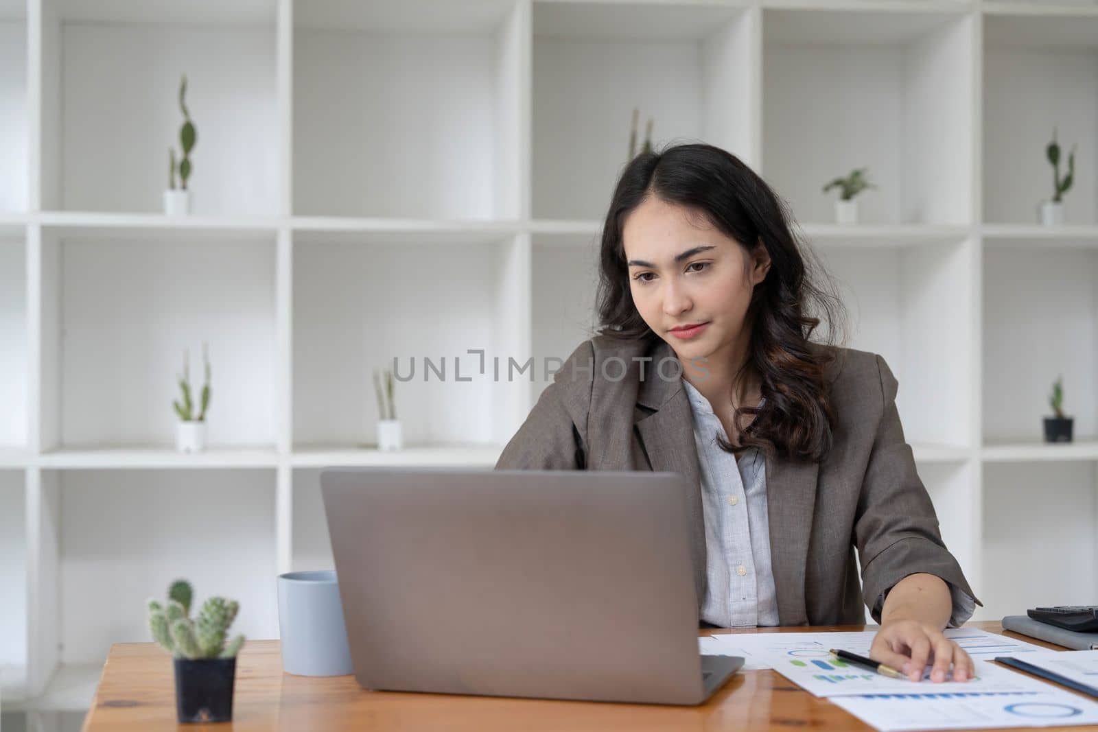 Portrait of serious young businesswoman accountant in formal wear sitting at her work place and use laptop, summarizing taxes, planning future investments, accounting at office...