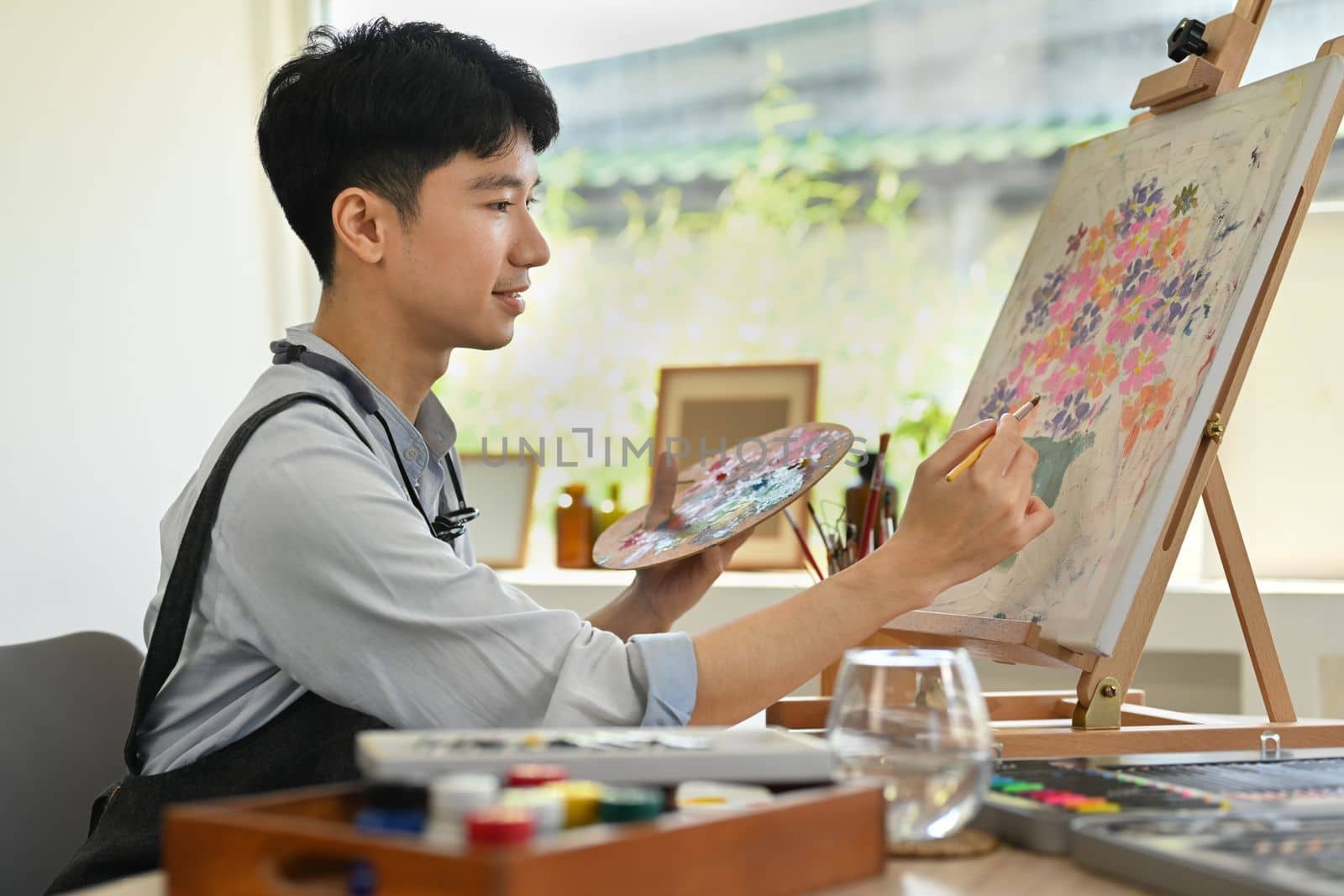 Image of pleased man artist painting picture with watercolor on canvas in art workshop. Art, creative hobby and leisure activity concept.