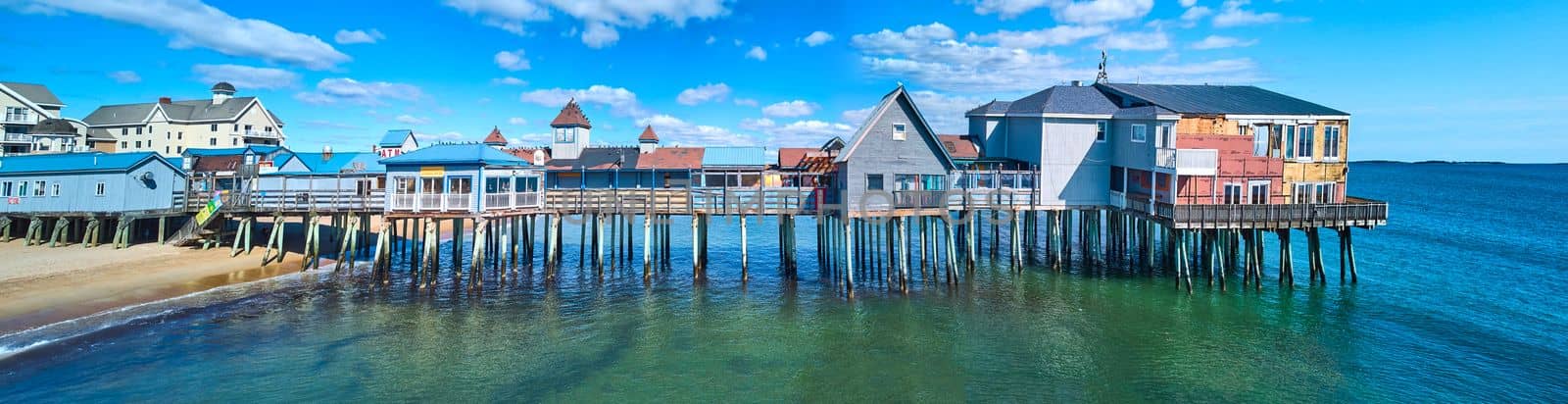 Image of Stunning side profile of entire old wood pier in Maine covered in shops and buildings on beach