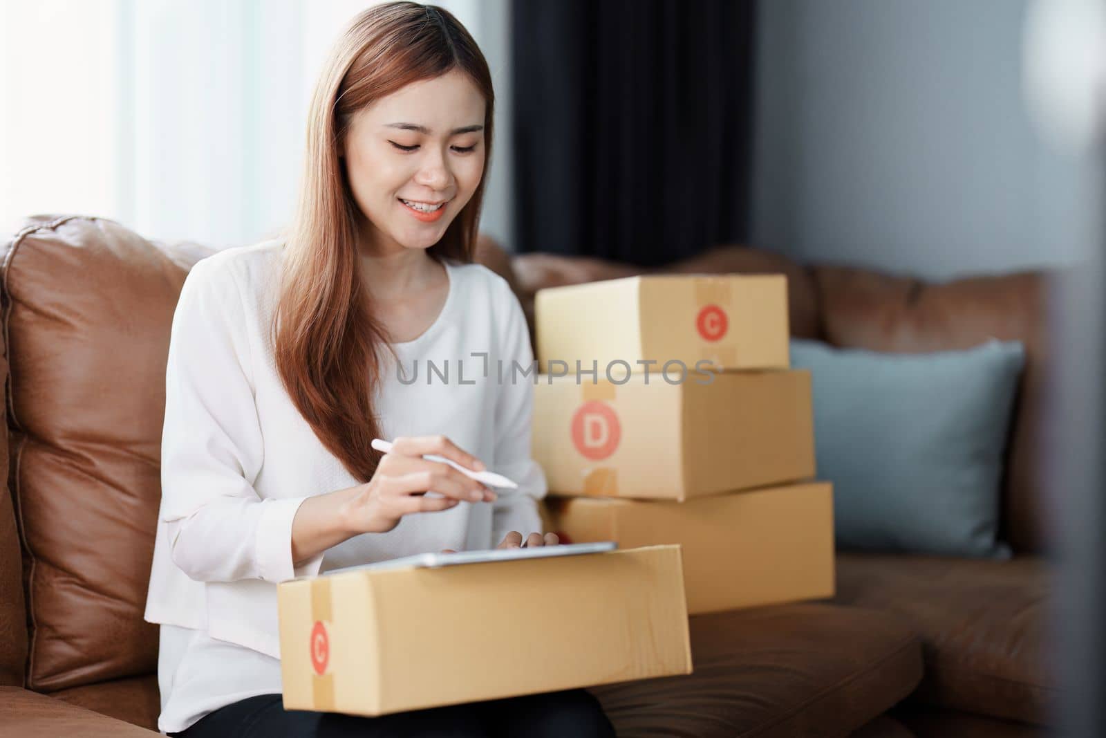 Starting small business entrepreneur of independent young Asian woman online seller is using tablet computer and taking orders to pack products for delivery to customers. SME delivery concept by Manastrong