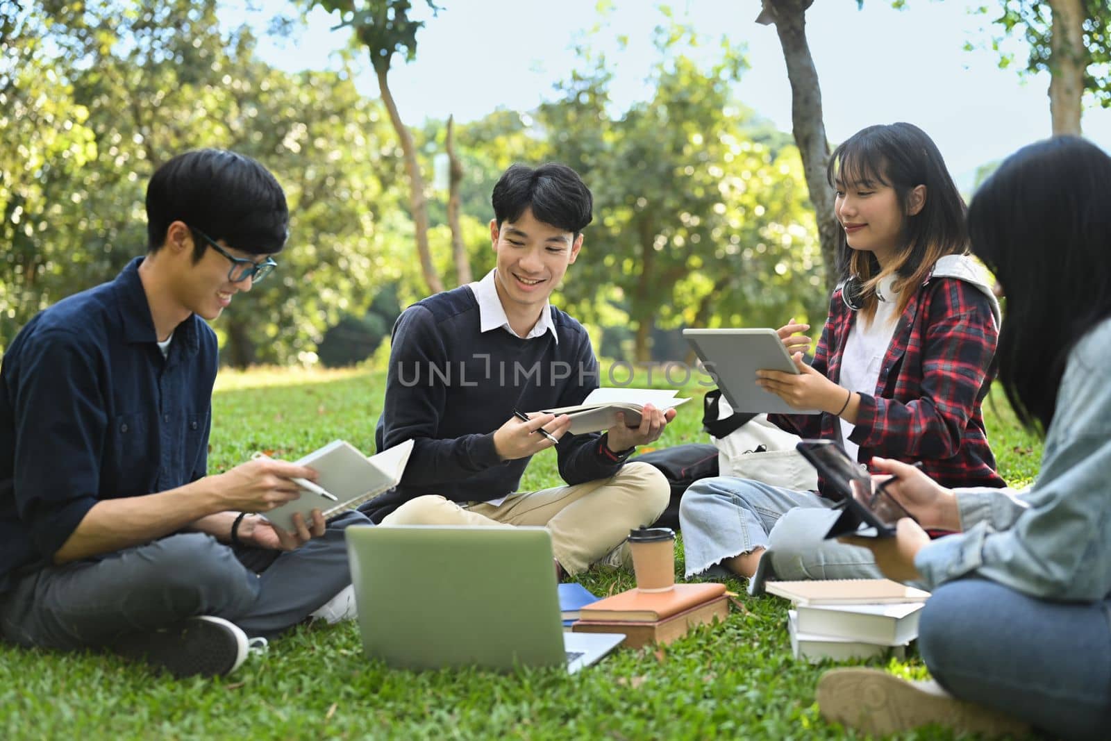 Group of university students reading book on green lawn at university campus. Youth lifestyle, university and friendship concept by prathanchorruangsak
