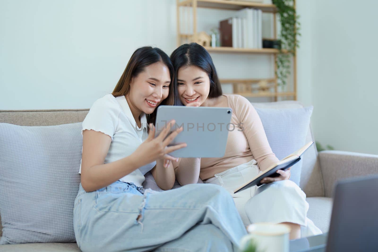 lgbtq, lgbt concept, homosexuality, portrait of two asian women posing happy together and loving each other while playing tablet at sofa by Manastrong