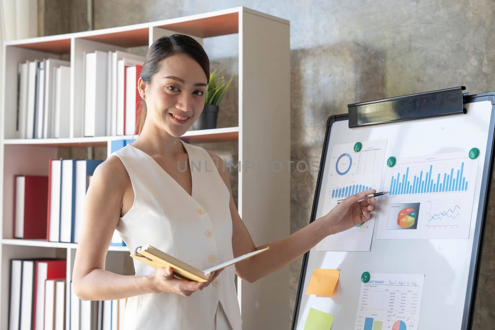 Young asian businesswoman in white suit pointing finger at large whiteboard presentation in the meeting...