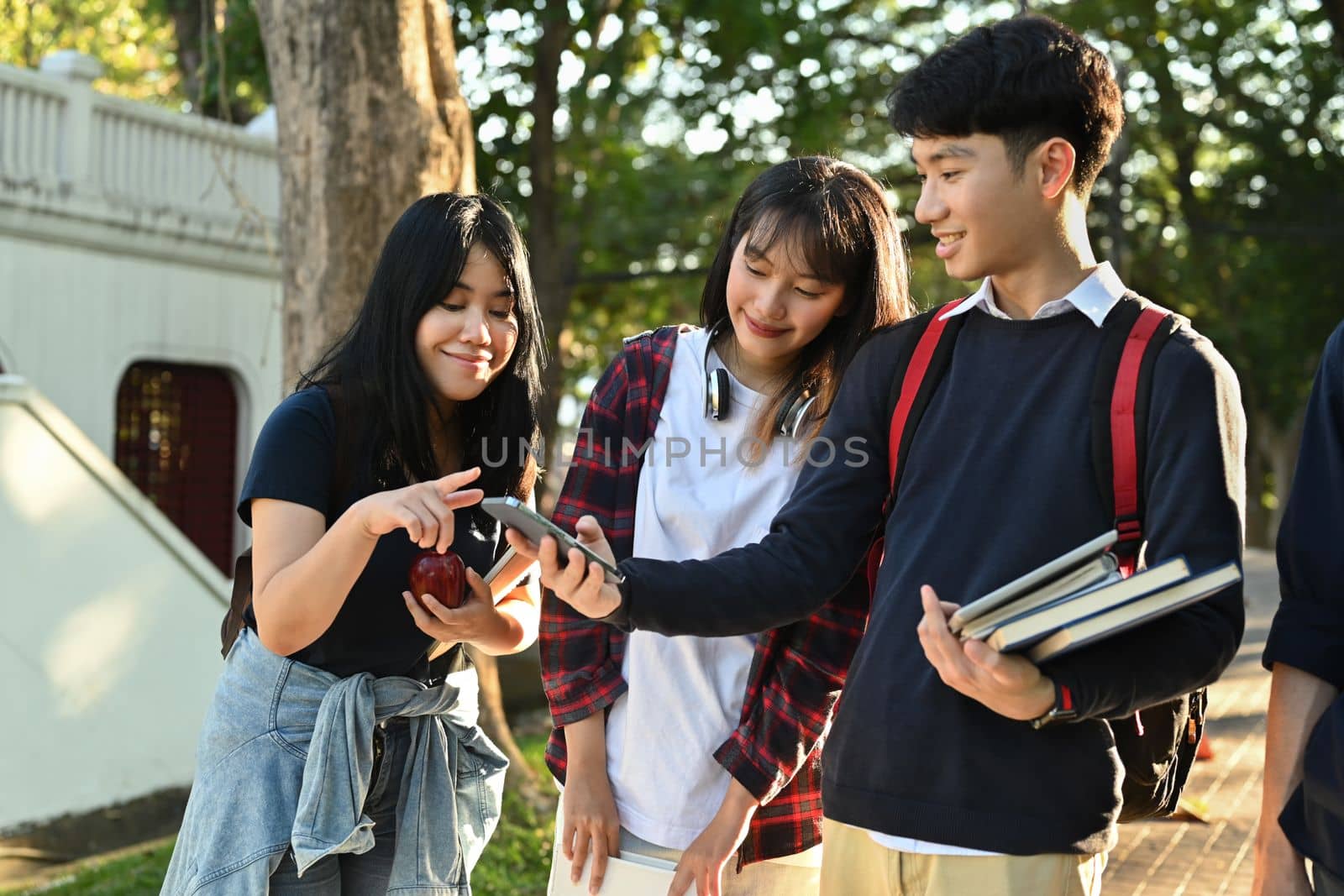 Group of asian students using mobile phone while walking together outdoors at university campus. Youth and community concept.