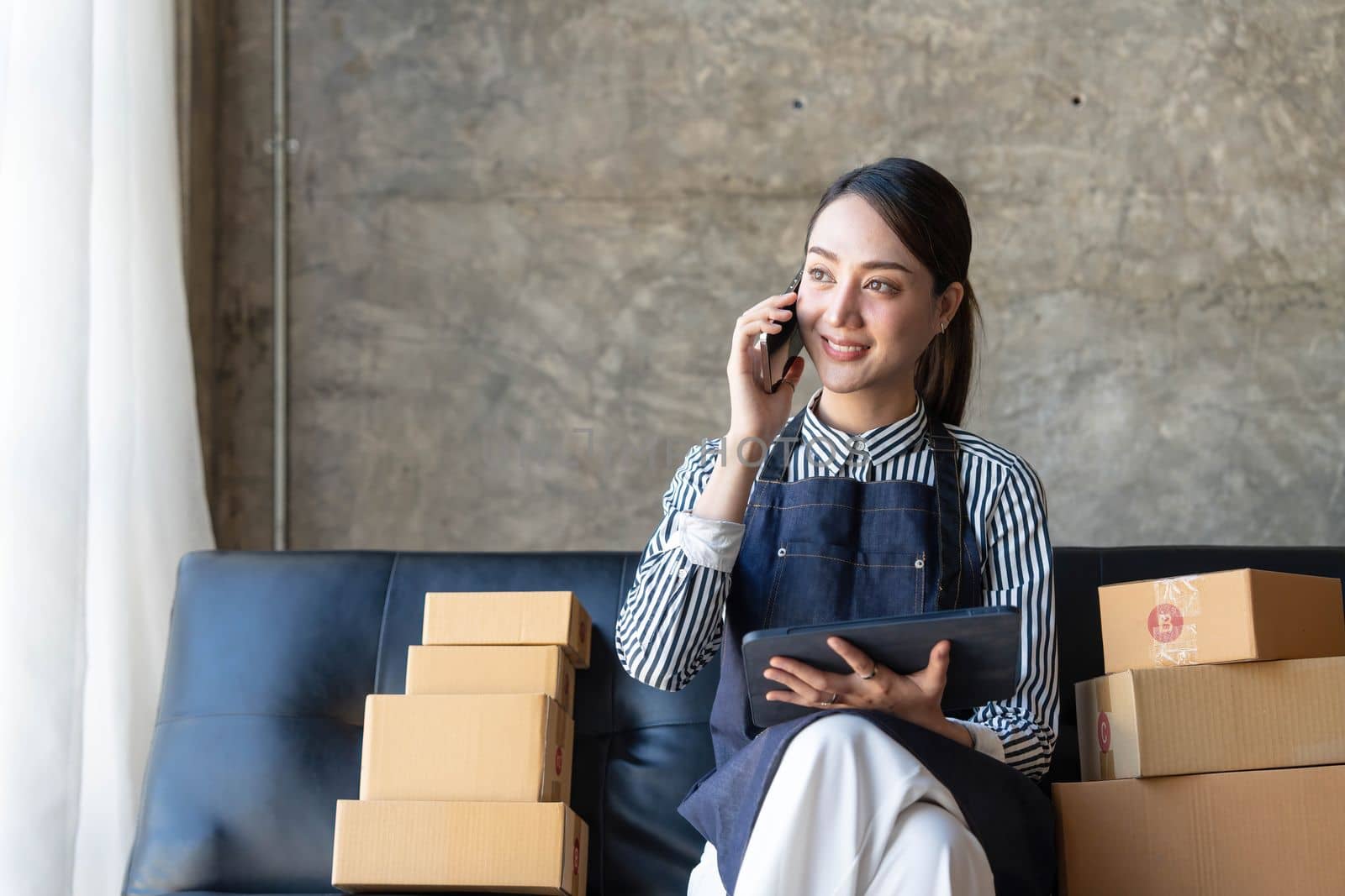 Startup small business entrepreneur SME freelance woman work with smart phone, Young Asian small business owner use computer, online market packing box delivery, SME e-commerce telemarketing concept..