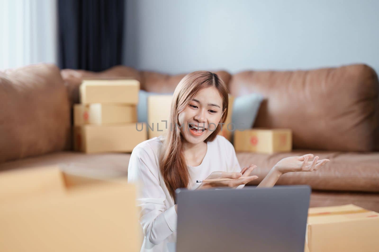 Starting small business entrepreneur of independent Asian female online seller talking on computer to video with a customer and packing products for delivery to the customer. SME delivery concept.