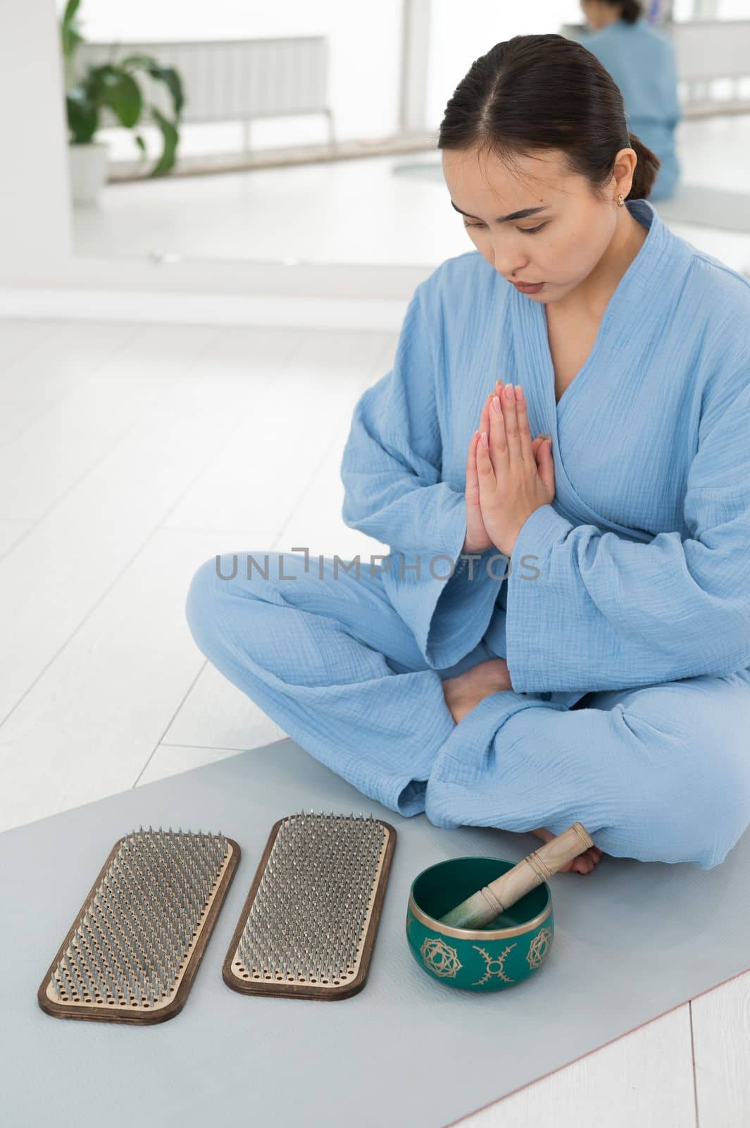 Asian woman sitting on yoga mat with tibetan singing bowl and sadhu boards