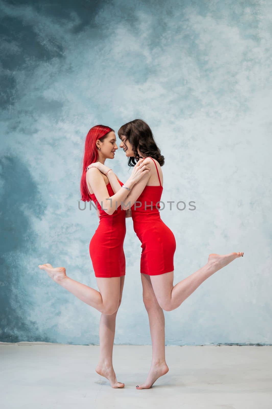 Full-length portrait of two tenderly embracing women dressed in identical red dresses. Lesbian intimacy
