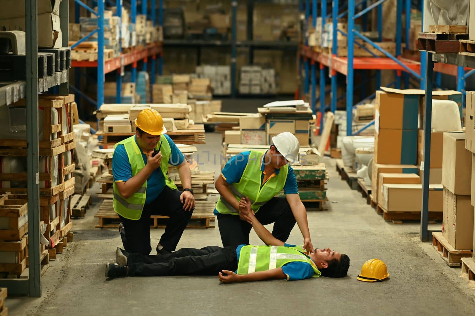 Two industrial worker are helping and giving the injured first aid to man lying unconscious on concrete floor.