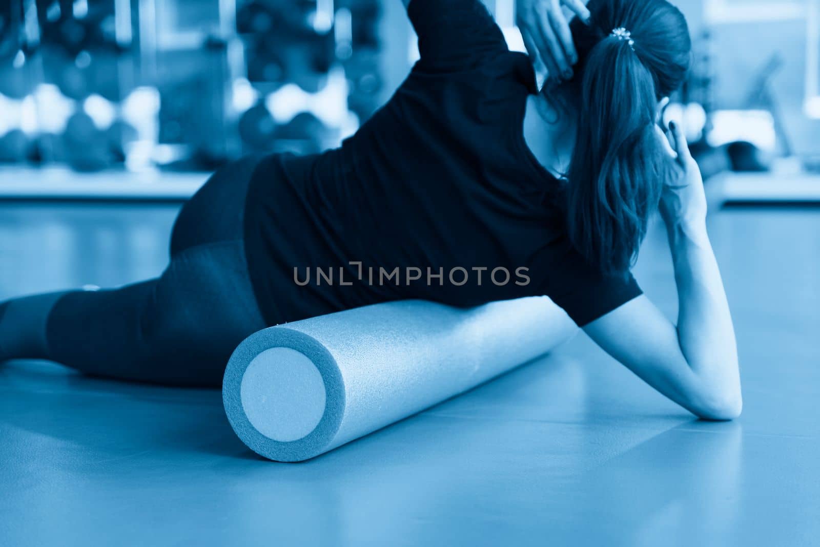Attractive female doing foam roller exercise and posing in modern bright fitness center