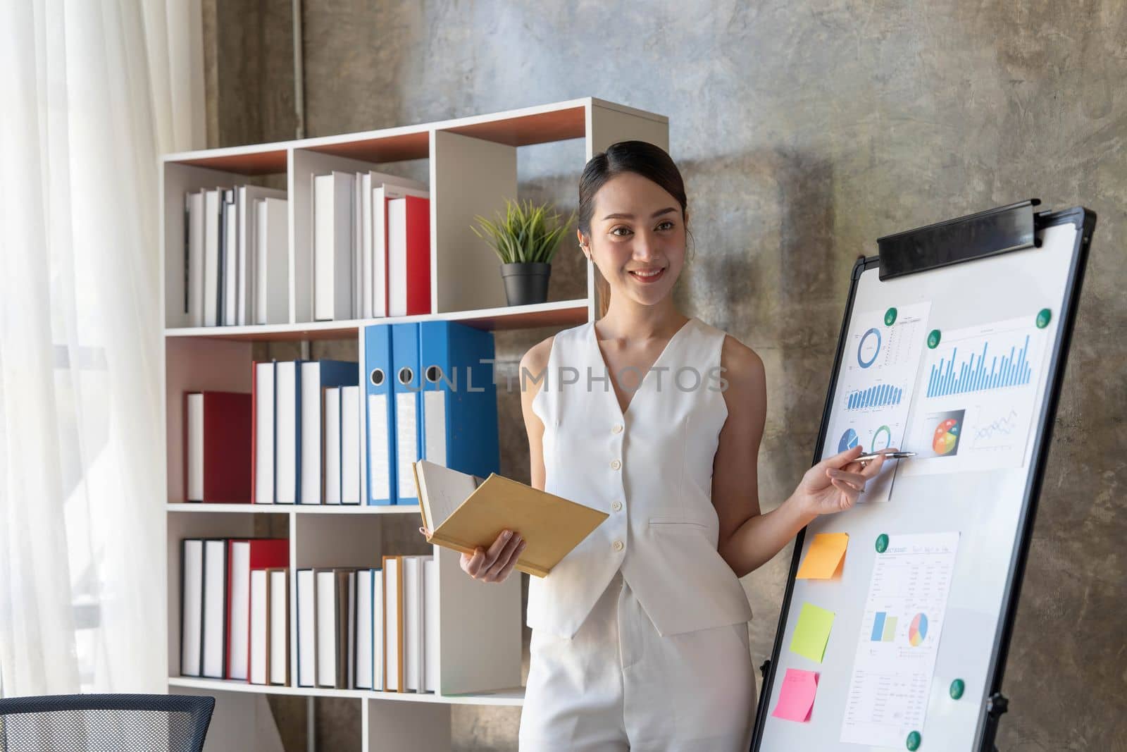Young asian businesswoman in white suit pointing finger at large whiteboard presentation in the meeting...