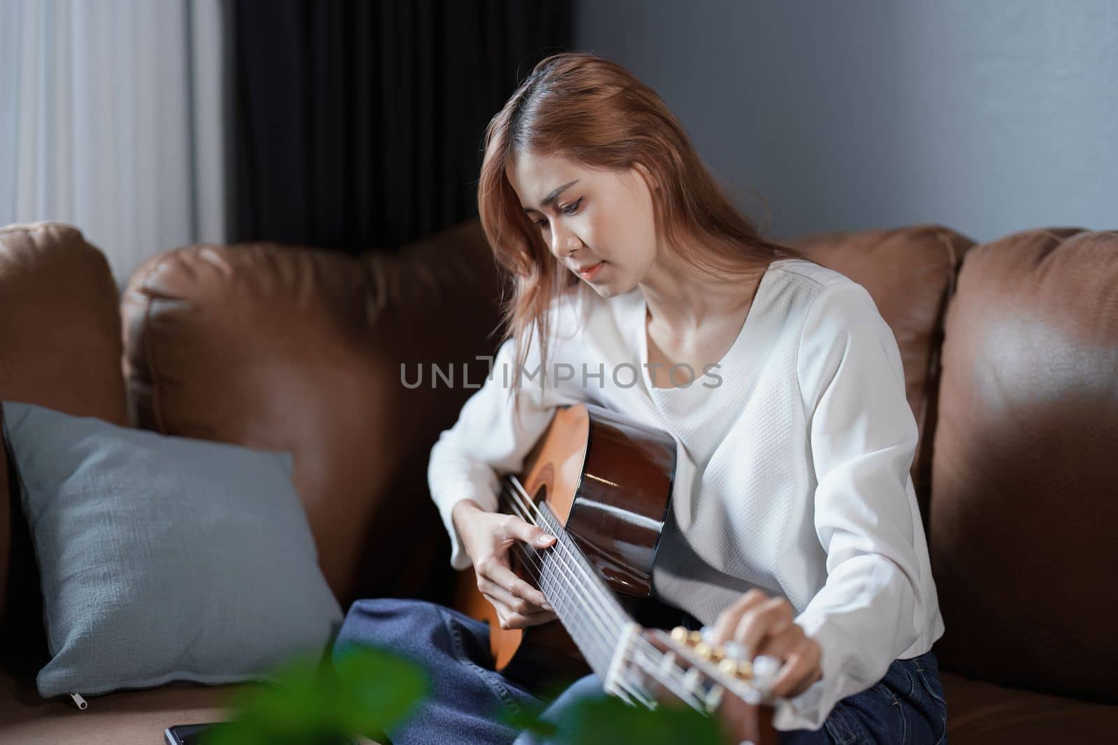 Portrait of young asian woman playing guitar on sofa relaxing stress on vacation by Manastrong