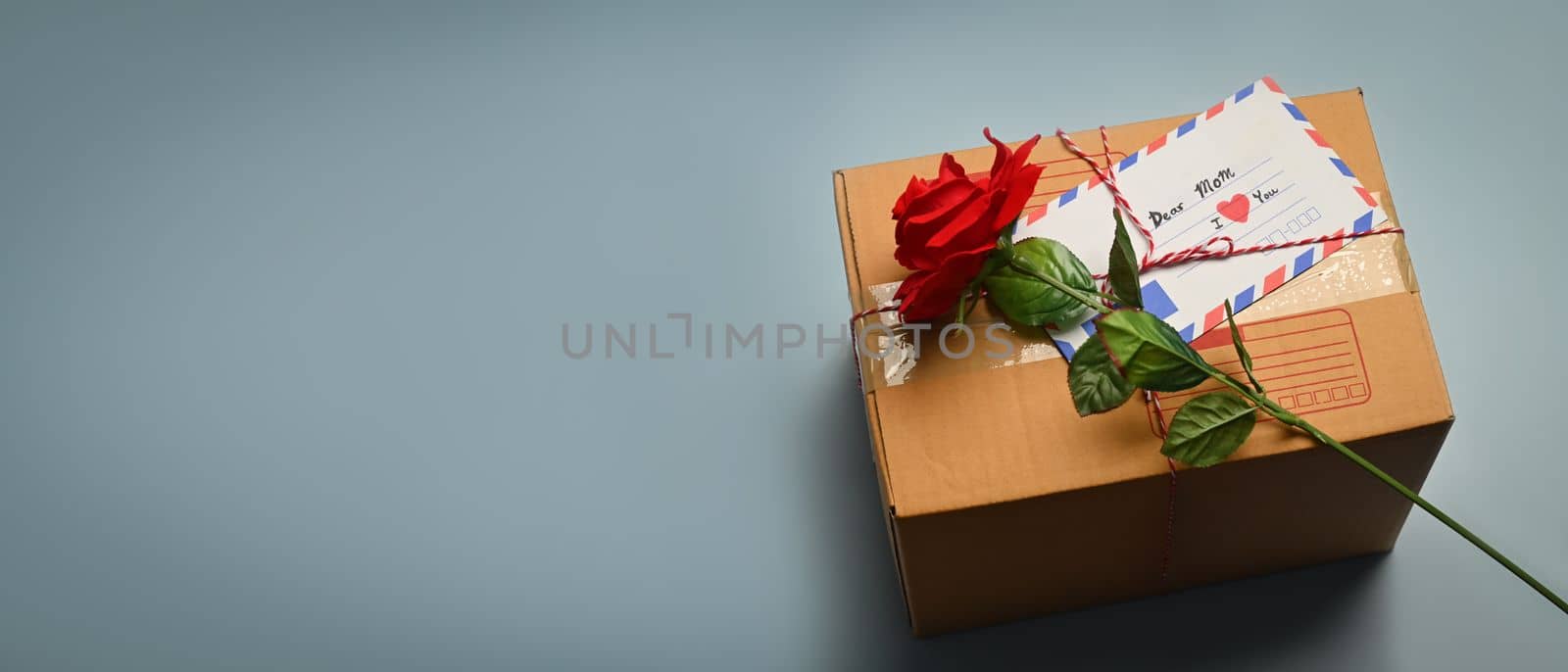 Gift boxes with greeting card and rose on blue background with copy advertising space. Preparation for holidays.
