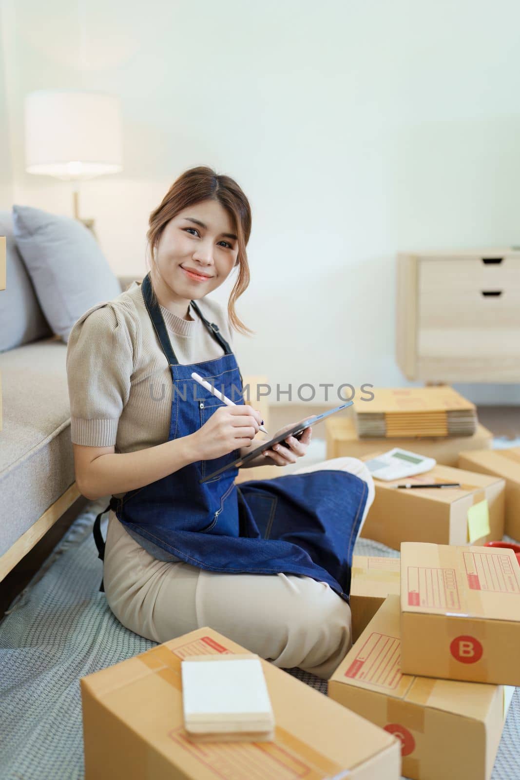 Starting small business entrepreneur of independent young Asian woman online seller is using smart phone and taking orders to pack products for delivery to customers. SME delivery concept.