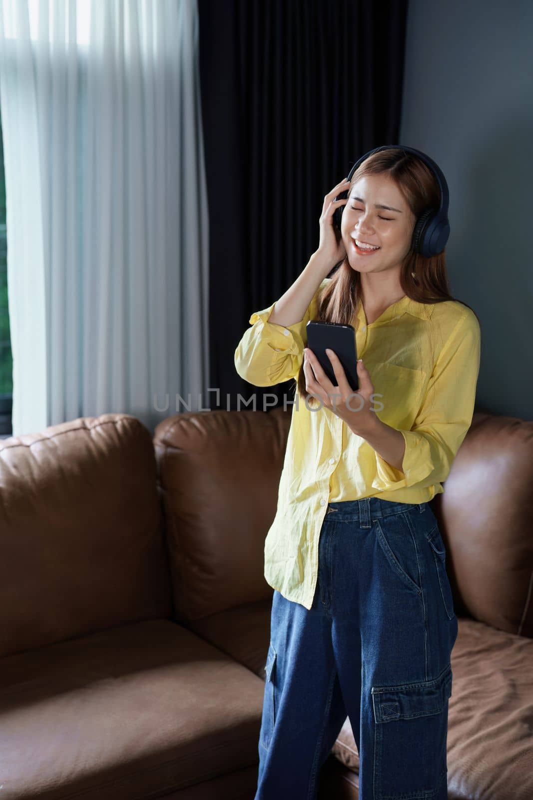 Portrait of asian woman using smart phone mobile and headphones relaxing on sofa at home.
