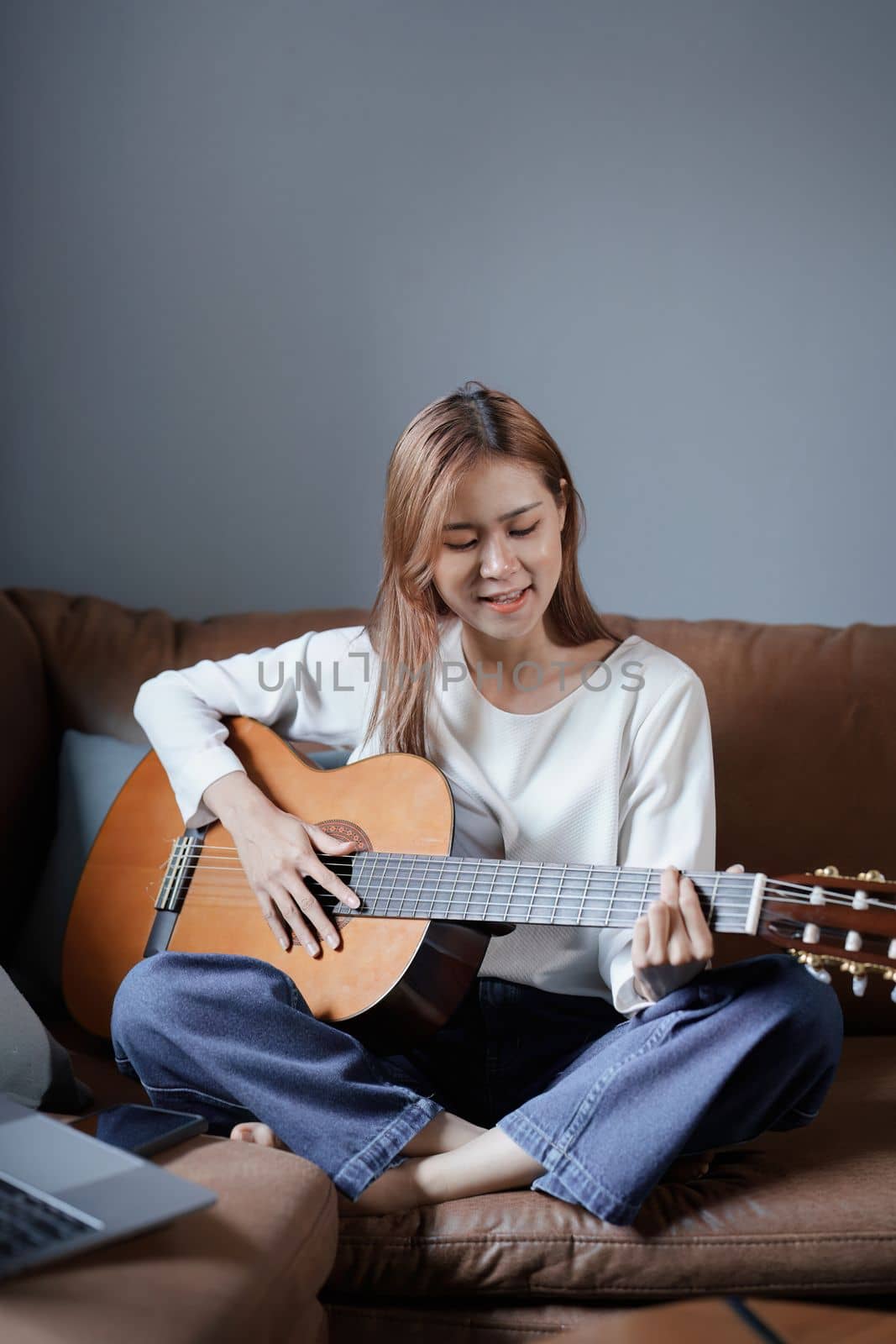 Portrait of young asian woman playing guitar on sofa relaxing stress on vacation.