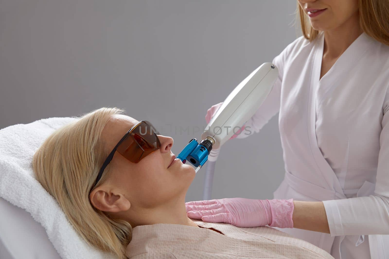 Middle aged Woman receiving laser treatment in cosmetology clinic wearing protective glasses by Mariakray