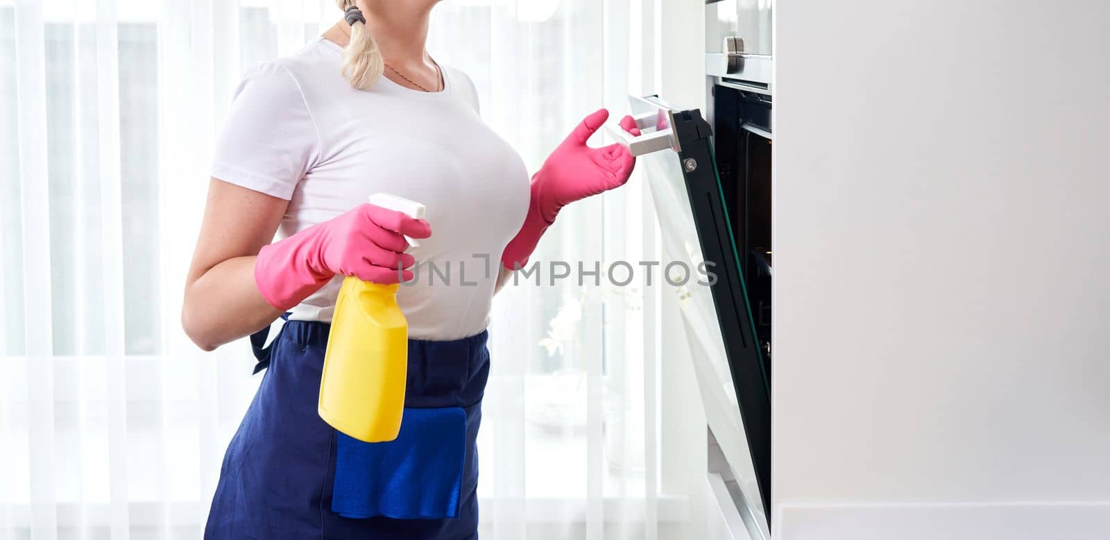 Young woman wearing gloves cleaning oven in the kitchen. Cleaning service concept by Mariakray