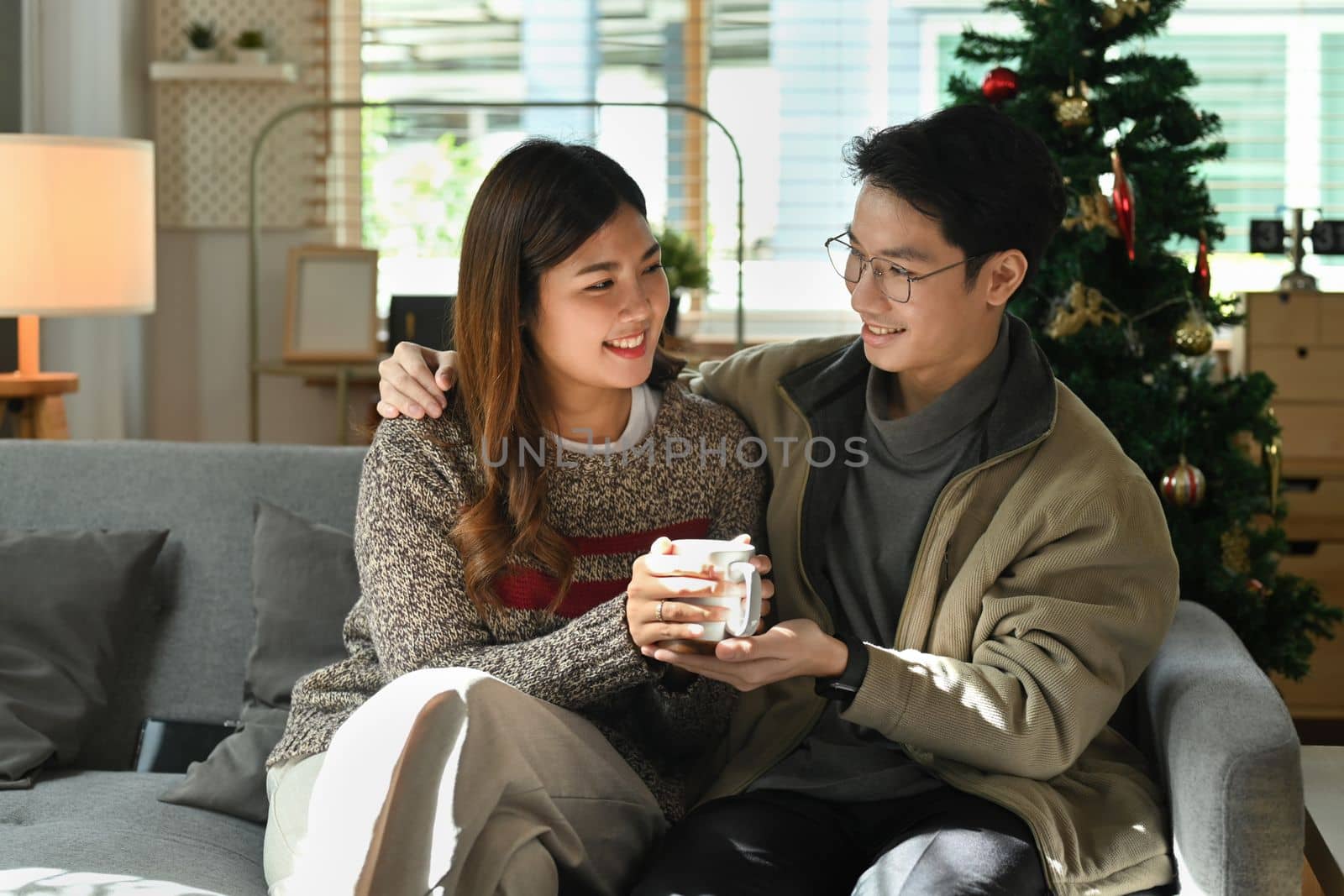 Romantic couple relaxing on comfortable couch, drinking hot chocolate and enjoying winter morning at home.