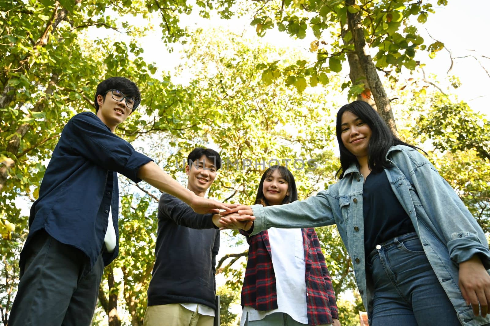 Image of young people celebrating together while stacking hands outdoor. Relationship youth and community concept.