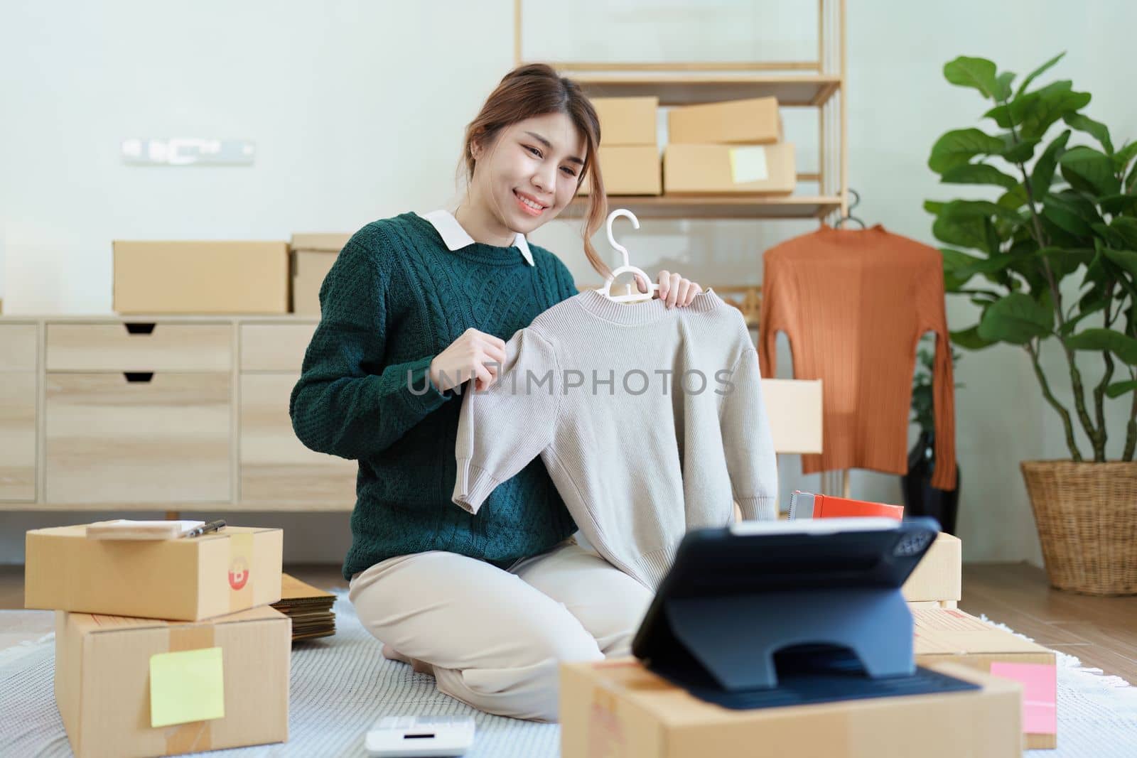Starting small business entrepreneur of independent young Asian woman online seller using a tablet computer showing products to a customer before making a purchase decision. SME delivery concept.