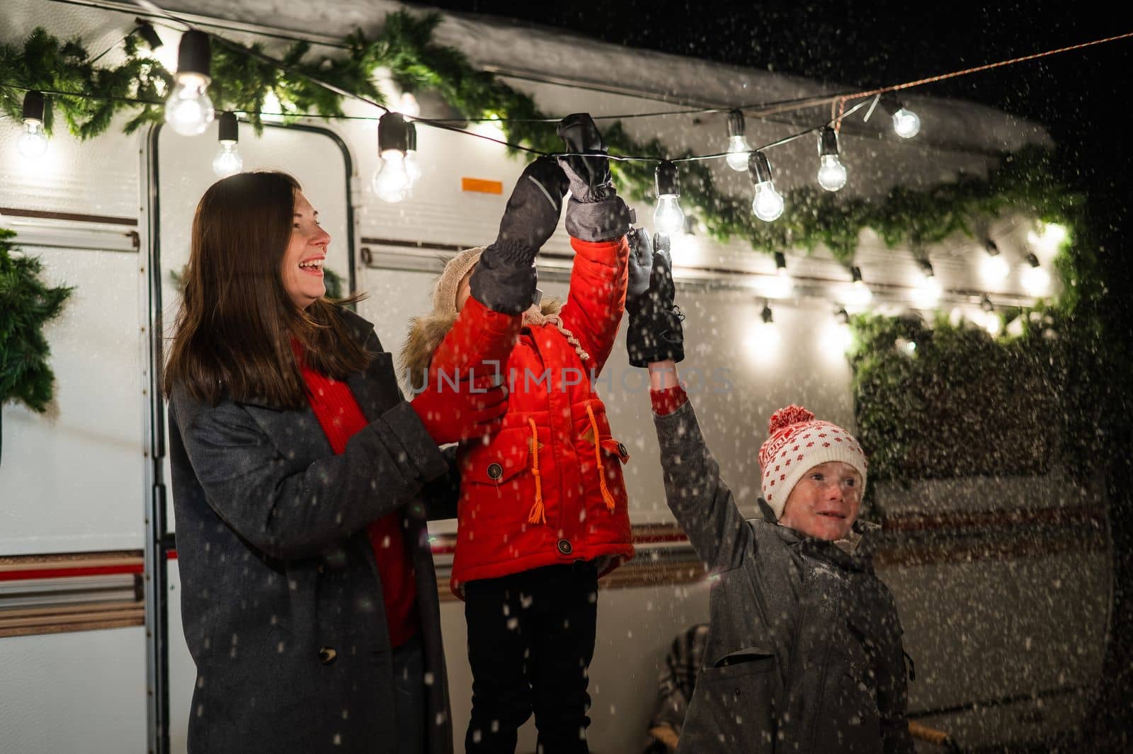Caucasian woman and two with sons celebrate Christmas in a camper. The mother of two boys decorates the van with Christmas lights