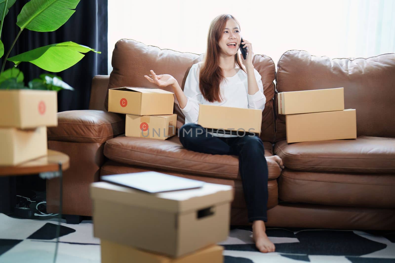 Starting small business entrepreneur of independent Asian female online seller talking on the phone with a customer and packing products for delivery to the customer. and SME delivery concept by Manastrong