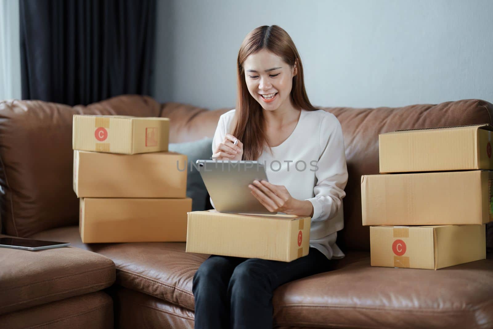 Starting small business entrepreneur of independent young Asian woman online seller is using tablet computer and taking orders to pack products for delivery to customers. SME delivery concept.