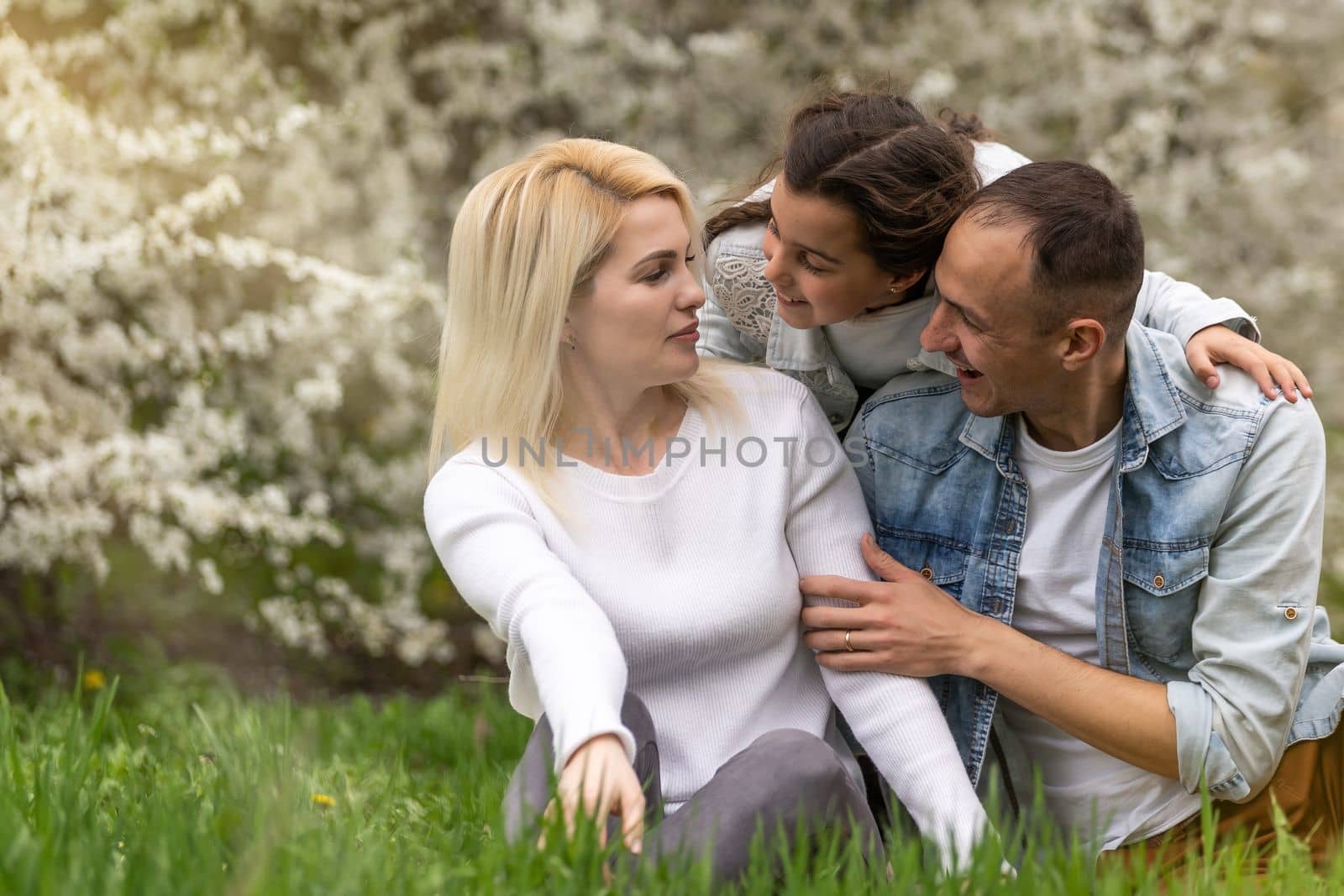 Happy family outdoors spending time together. Father, mother and daughter are having fun on a green floral grass