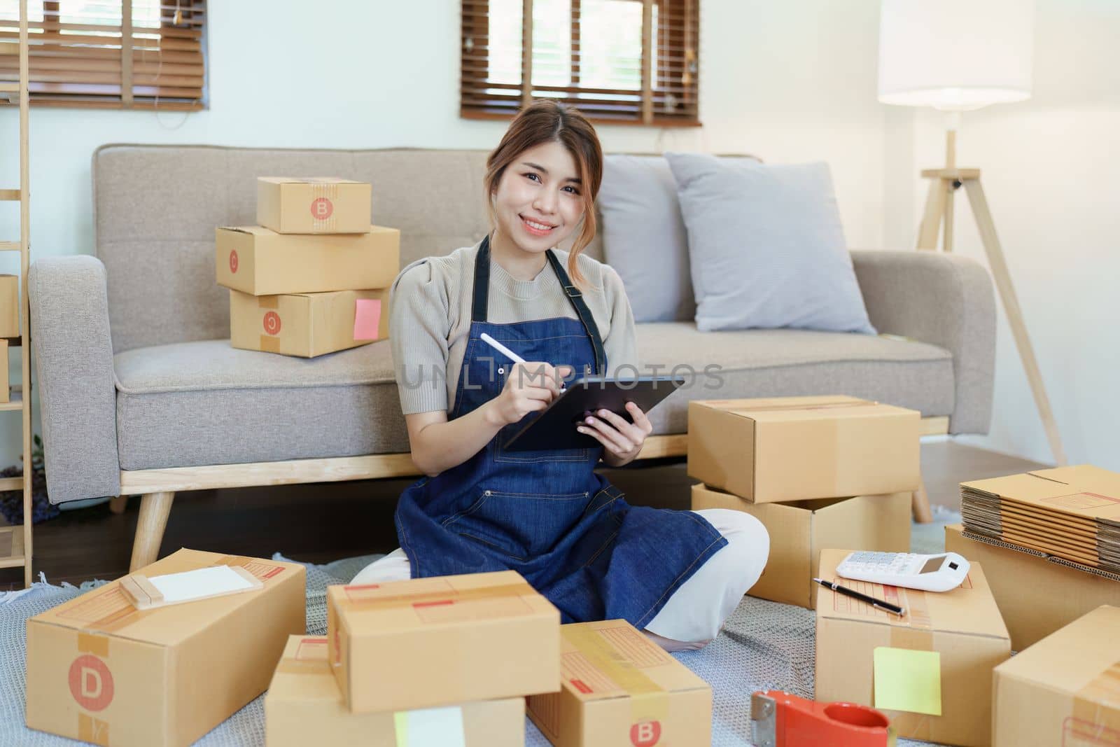 Starting small business entrepreneur of independent young Asian woman online seller is using smart phone and taking orders to pack products for delivery to customers. SME delivery concept.