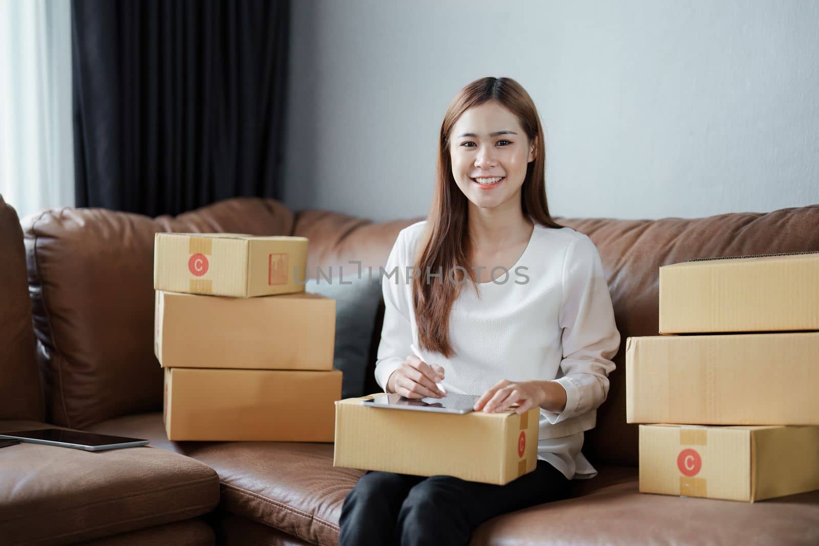 Starting small business entrepreneur of independent young Asian woman online seller is using tablet computer and taking orders to pack products for delivery to customers. SME delivery concept by Manastrong